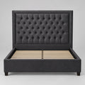 A dark gray tufted velvet headboard leaning against a plain white wall.