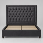 A dark gray tufted velvet headboard leaning against a plain white wall.