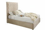 A modern upholstered bed with a tall, pleated beige headboard and matching footboard, styled with white bedding, patterned pillows, and a cream throw blanket in a bright bedroom.